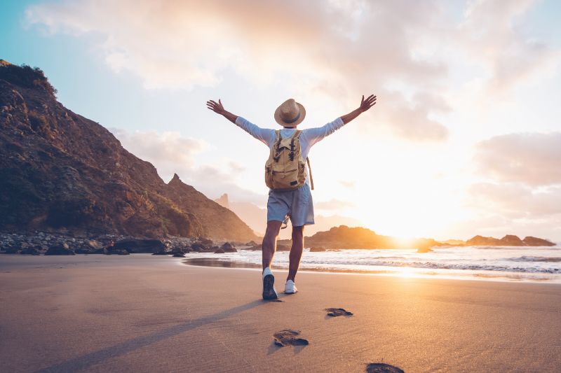 male standing on a sandy beach with arms up in the air